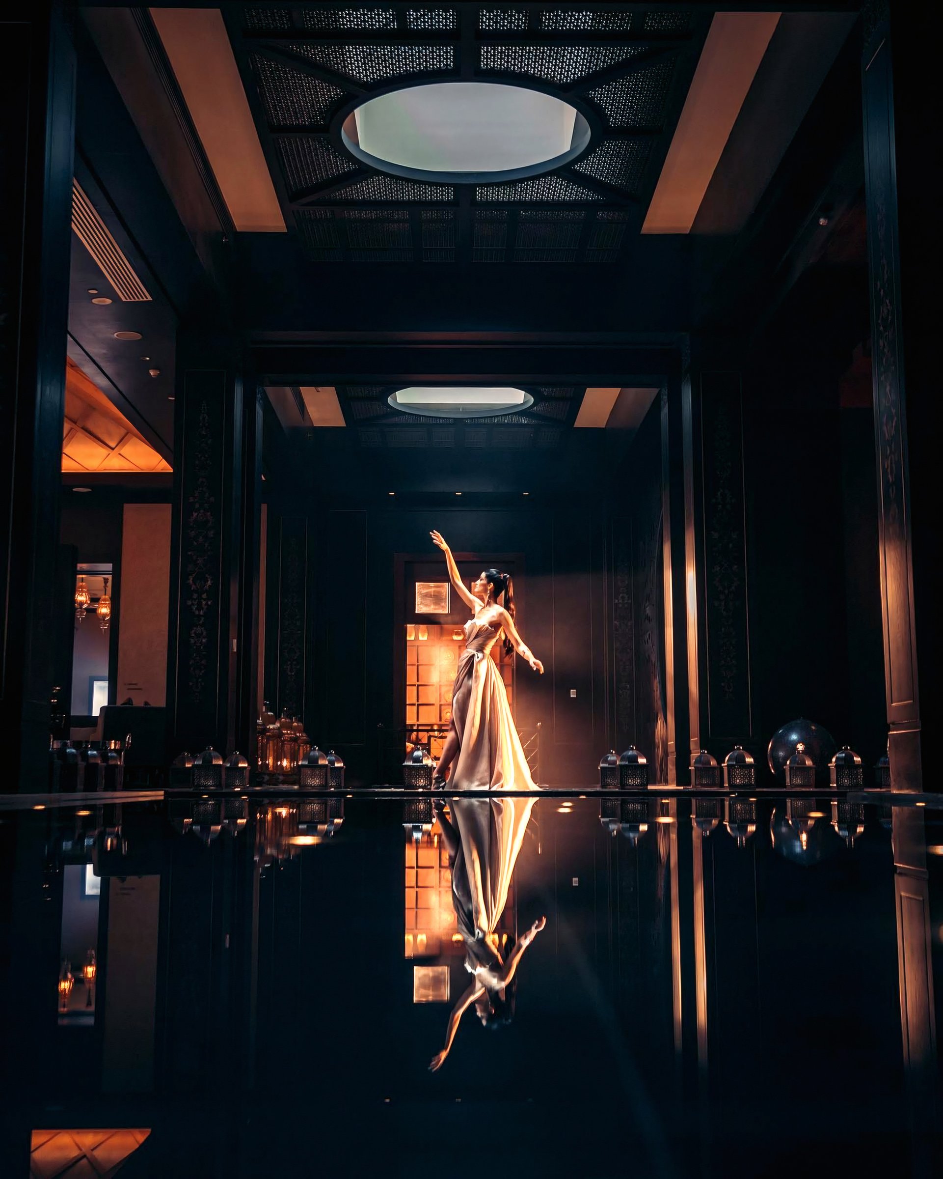 A woman illuminated at the end of an ornate dark corridor.