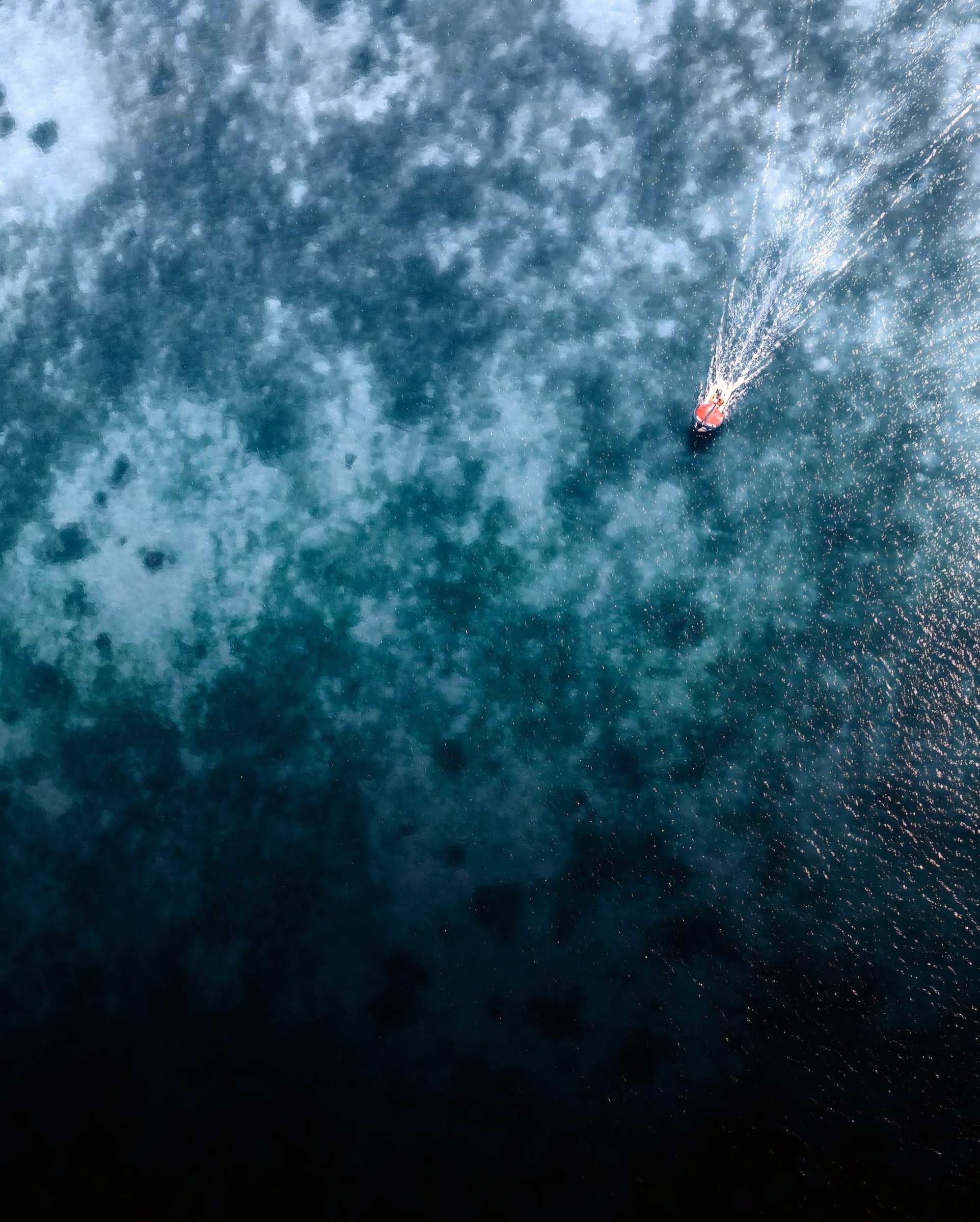A small boat crossing patterned blue reef water.