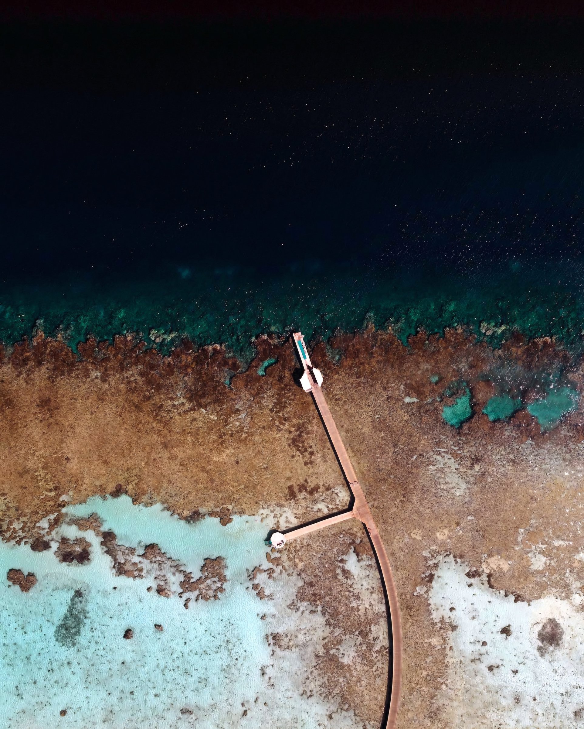 Aerial view of a walkway extending across shallow reef water.
