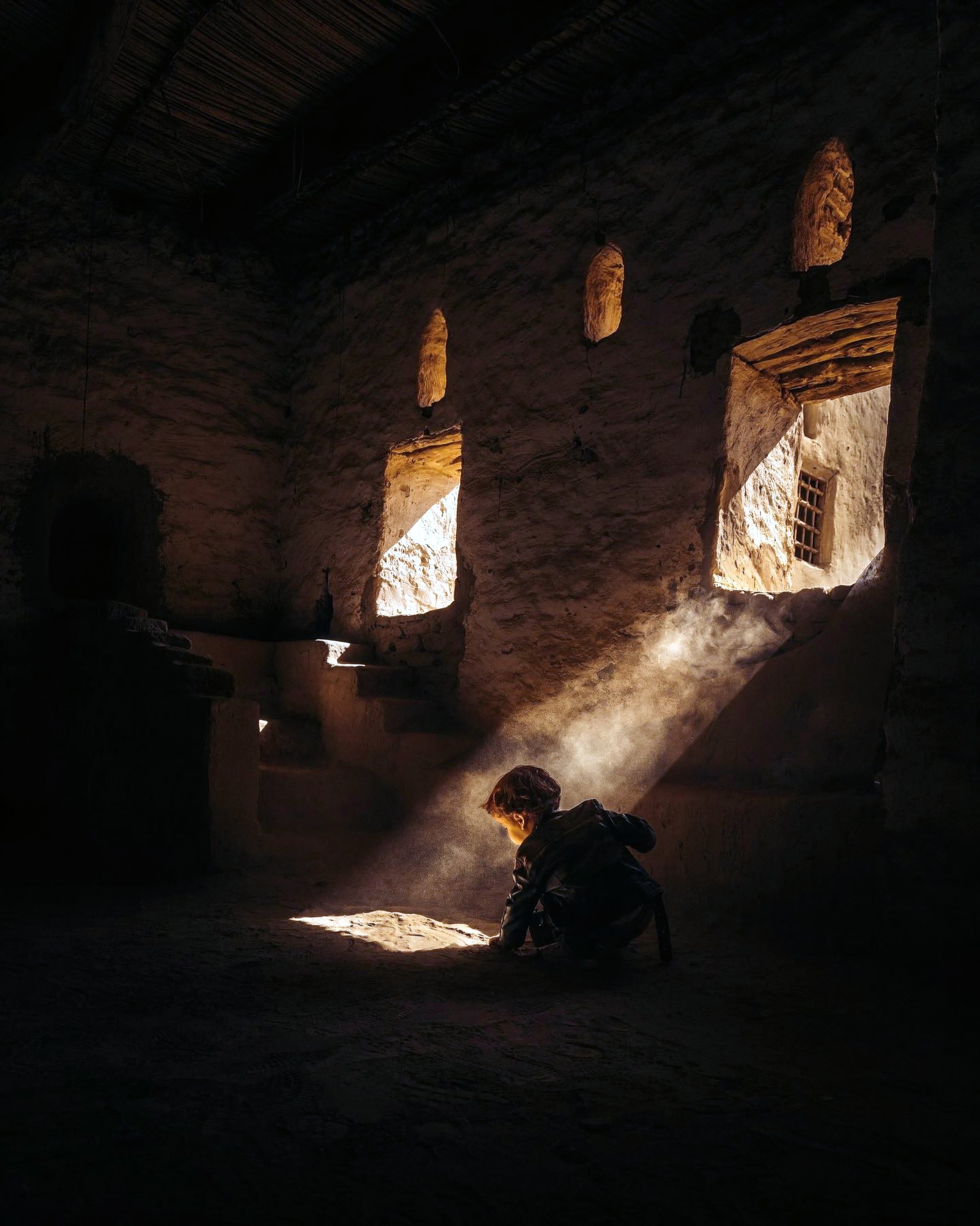 A person in a dim stone interior with narrow shafts of light.