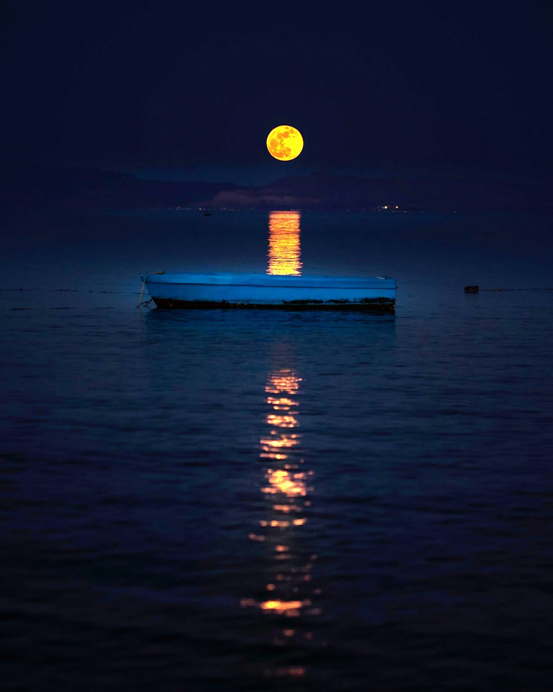 A yellow moon above a boat on dark blue water.