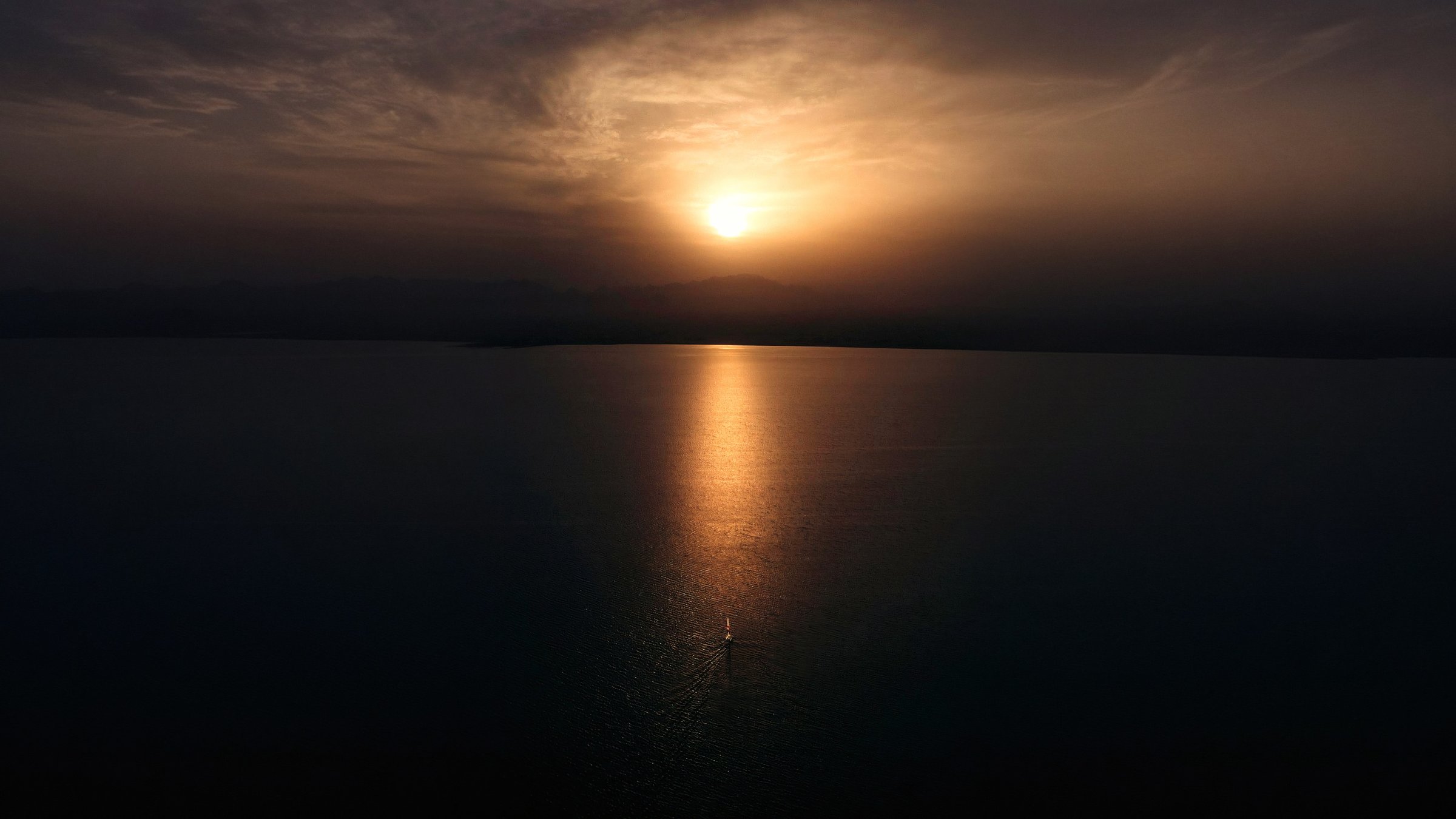 A golden sun and reflection stretching across calm dark water.