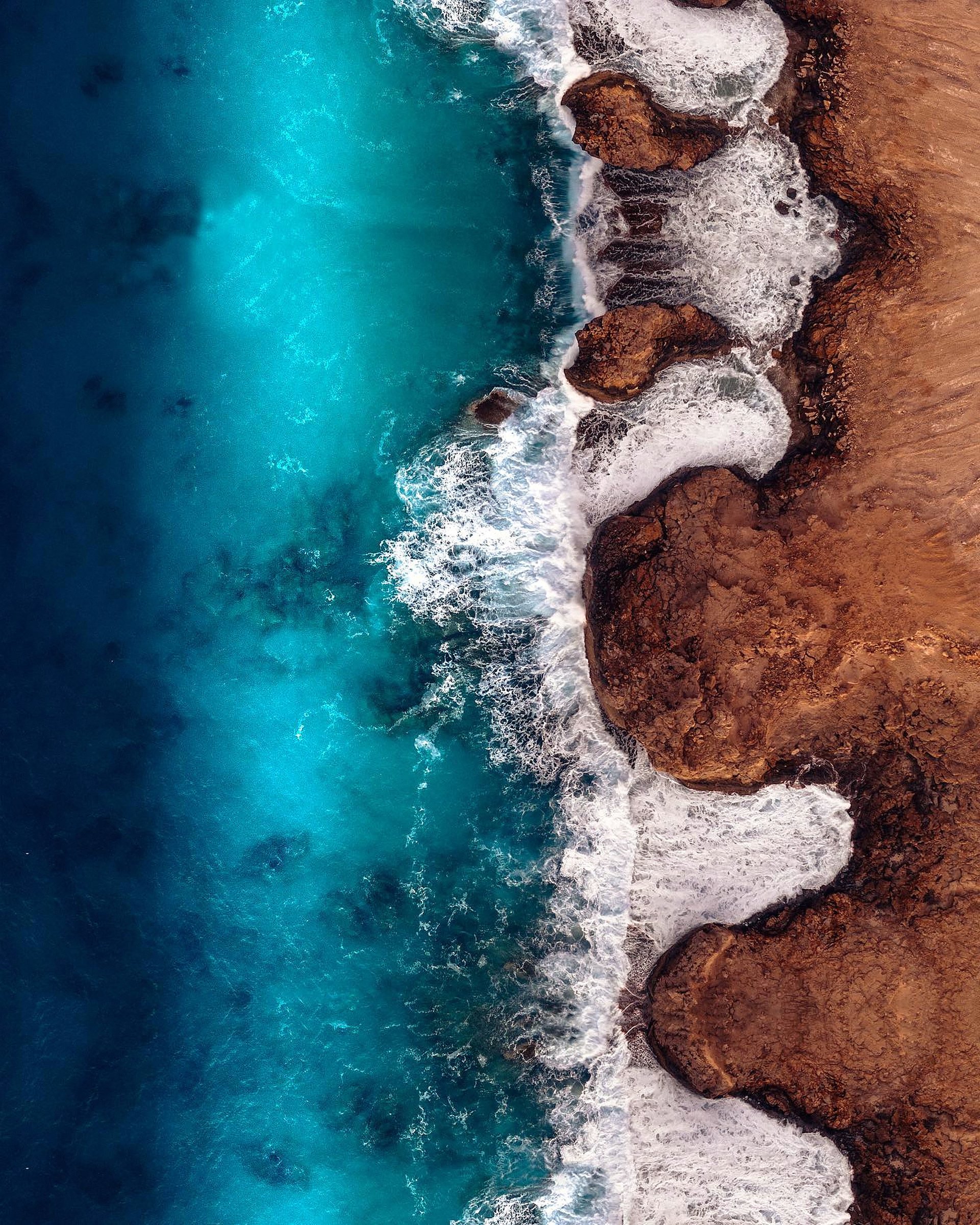 An aerial view of waves meeting a rugged coastline.