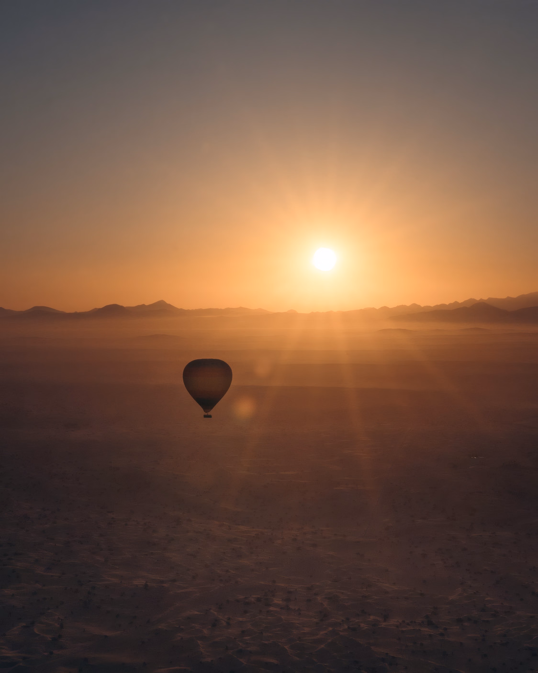A hot-air balloon over a hazy landscape at sunrise.