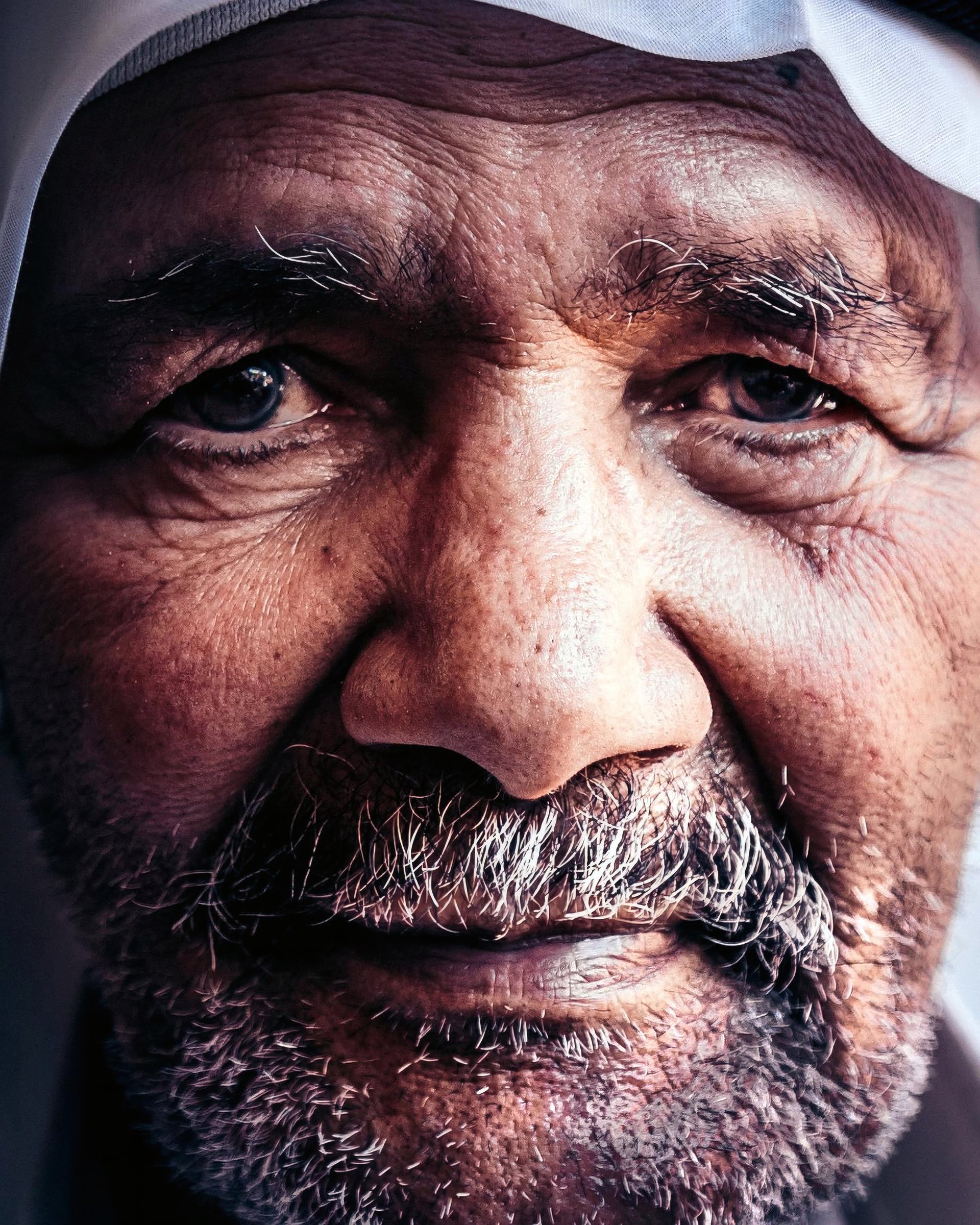 Close portrait of an older man wearing a traditional head covering.